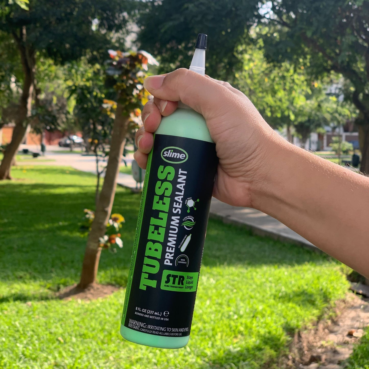 Mano sosteniendo sellador Slime Tubeless Premium en un parque.