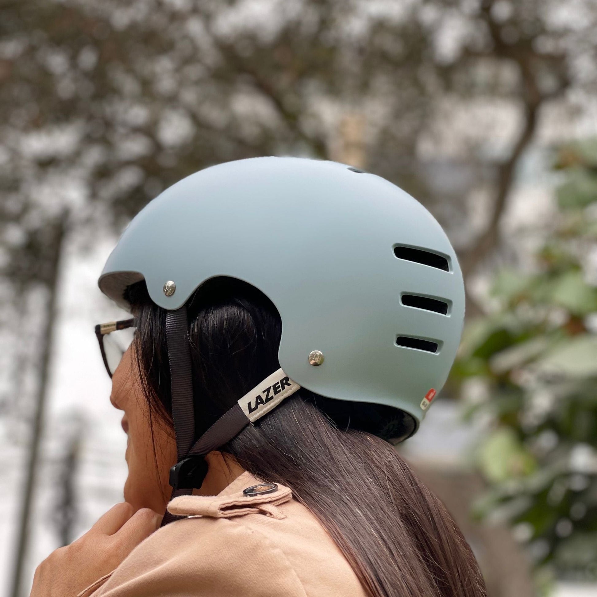Mujer usando el Casco Lazer One Plus de color celeste claro, disfrutando de un paseo al aire libre en un entorno natural.